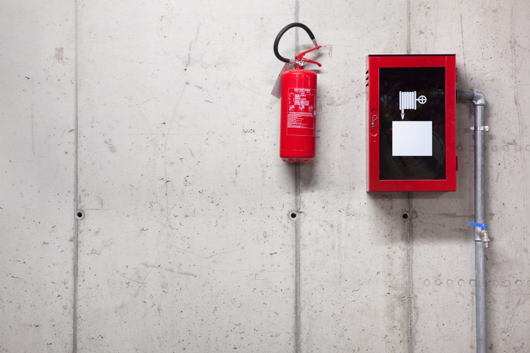 A fire extinguisher and a fire-hose on concrete wall Fire extinguisher